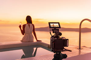 Video camera filming actress woman acting for movie on luxury hotel location behind the scenes of shoot. Professional videography equipment shooting outdoor at sunset.